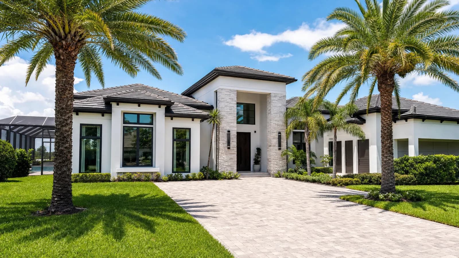 Luxurious modern Orlando home with a white stucco facade, palm trees, a manicured lawn and a wide paver driveway under a blue Florida sky